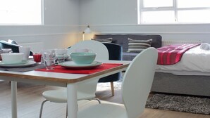 Een moderne, goed verlichte kamer met een eettafel voor twee personen, een bank en een bed.