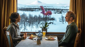 Two people dining at a table with a view of a snowy landscape and a mountain in the background. - Venabu Fjellhotell (Ringebu)