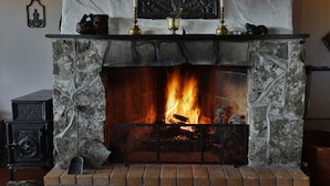 A fireplace with a stone surround, a mantel with decorative items, and a lit fire. - Venabu Fjellhotell (Ringebu)