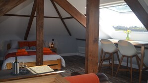 A cozy attic bedroom with a bed, a small table with wine glasses, and a dining area with chairs. - Appledore Factory (Bideford)