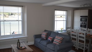 A living room with a grey sofa, a wooden coffee table, and a view of a body of water through large windows. - Appledore Factory (Bideford)