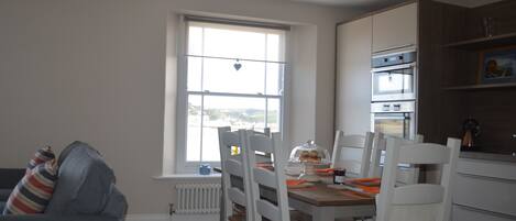 Cocina compacta con armarios blancos, una mesa de comedor con sillas y una ventana con vistas al exterior.