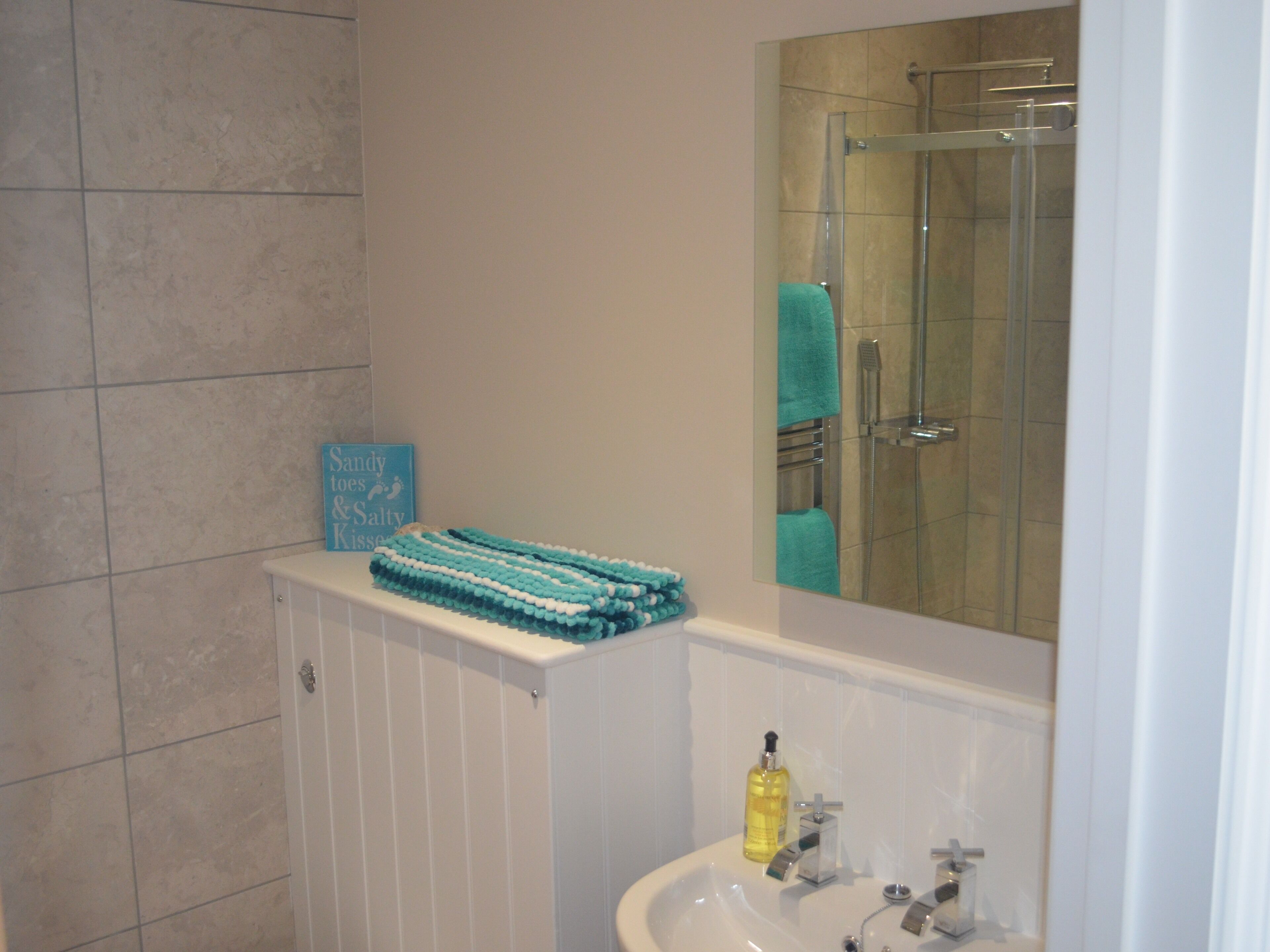 A bathroom with a white sink, a mirror, a glass shower enclosure, and a towel rack.