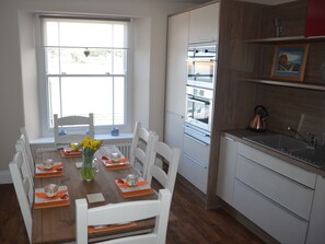 A modern kitchen with white cabinetry, a built-in oven, and a window with a view of the outside. - Appledore Factory (Bideford)