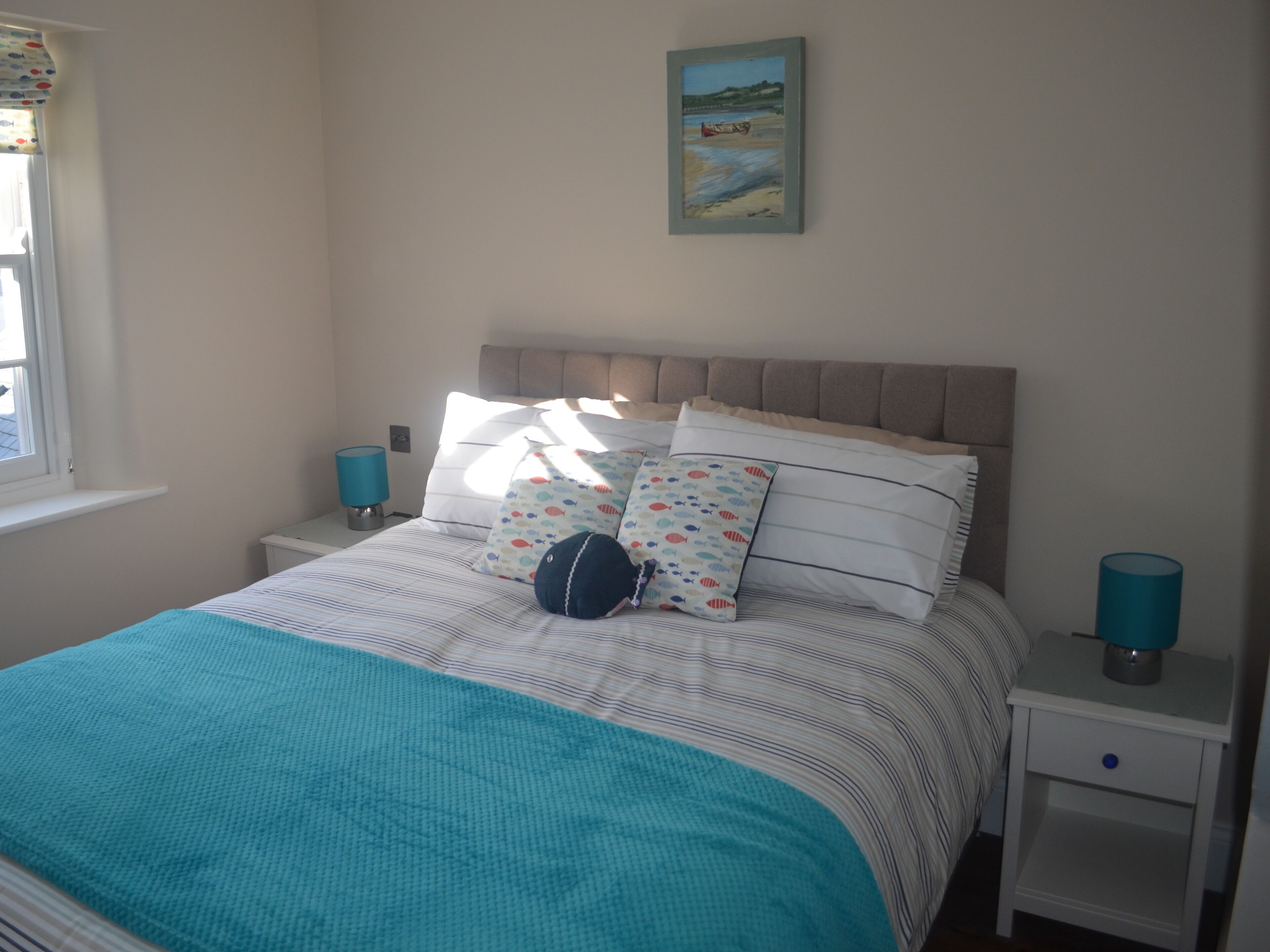 A bedroom with a bed, pillows, a nightstand, a lamp, and a painting on the wall.