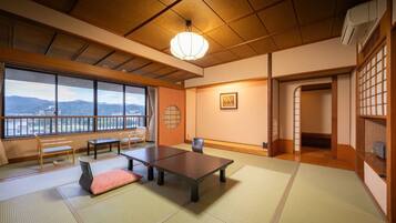 Habitació japonesa tradicional amb sòl de tatami, una taula baixa, una banca i vista a les muntanyes a través de grans finestres.