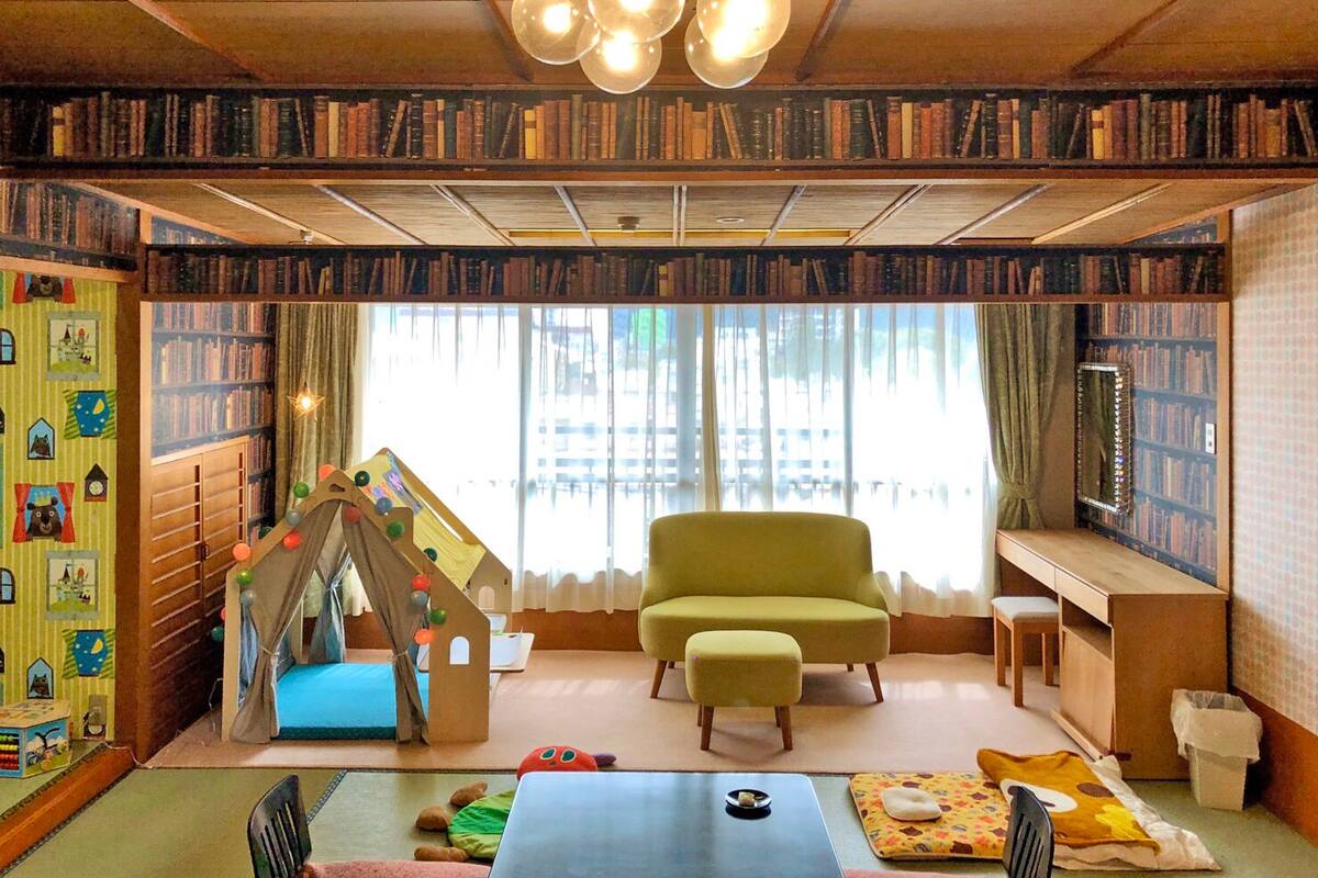 A cozy room with a bookshelf, a play tent, a green armchair, and a dining table.