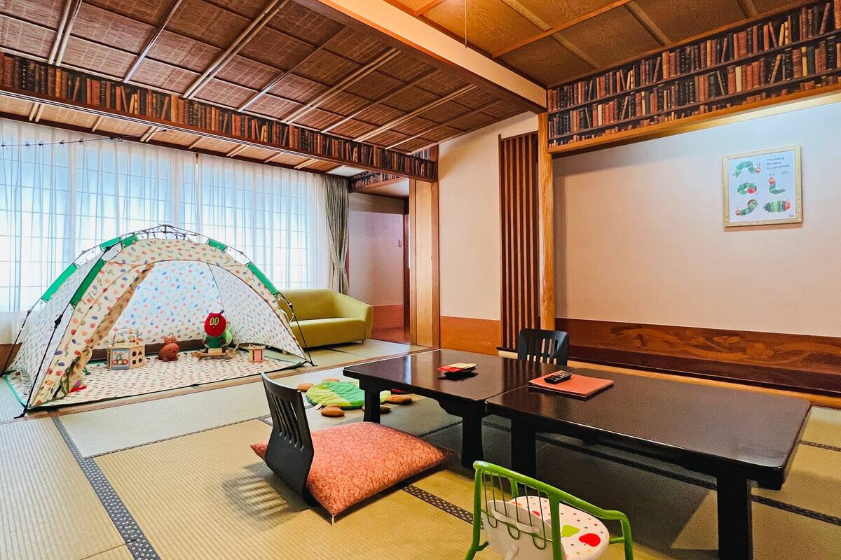 A traditional Japanese-style room with tatami flooring, a low table, chairs, and a bookshelf filled with books.