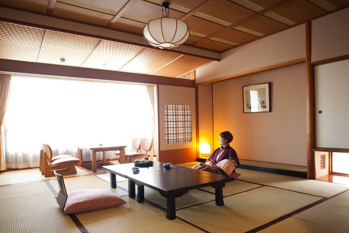 A traditional Japanese room with tatami flooring, a low table, and a person seated.
