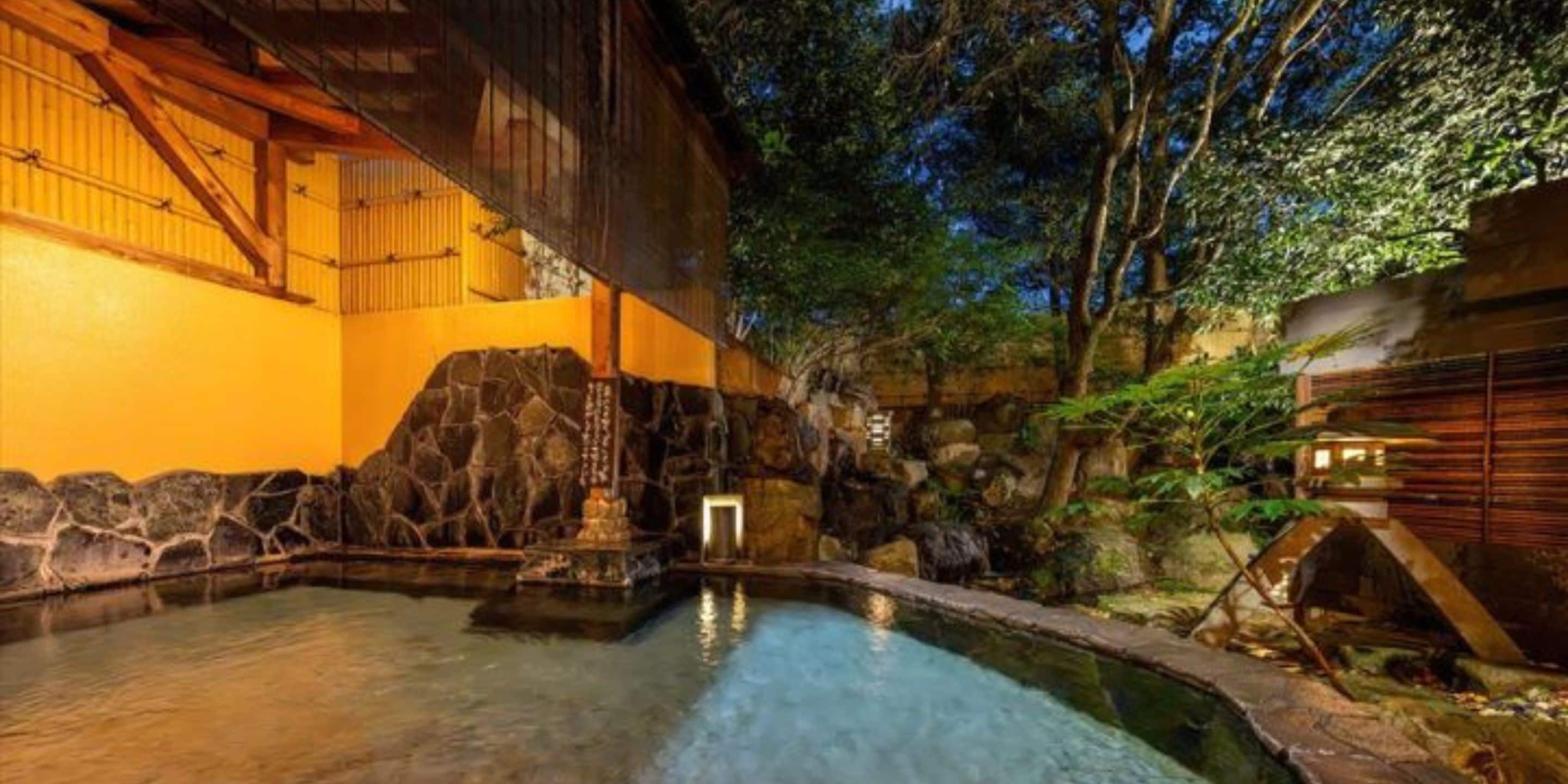 Een traditionele Japanse onsen met een stenen bad, houten architectuur en uitzicht op de omliggende bomen.