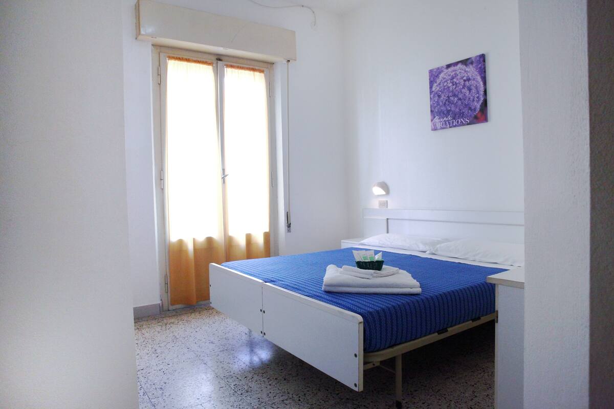 Un lit simple avec une couvre-lit bleue, des oreillers blancs et une petite table de chevet avec une lampe.