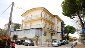 A multi-story residential building with balconies, a parking area, and a sidewalk. - Hotel Lagomaggio (Rimini)