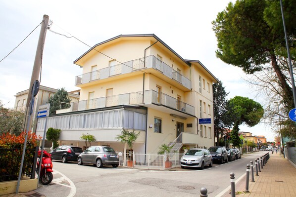 A multi-story residential building with balconies, a parking area, and a sidewalk. - Hotel Lagomaggio (Rimini)