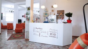 A reception area with a white desk, orange chairs, and a patterned rug. - Hotel Lagomaggio (Rimini)