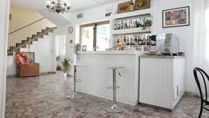 A bar area with two stools, a counter with bottles, a television, and a staircase in the background. - Hotel Lagomaggio (Rimini)