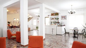 A spacious living area with a kitchen in the background, featuring a bar and dining area with chairs and a table. - Hotel Lagomaggio (Rimini)
