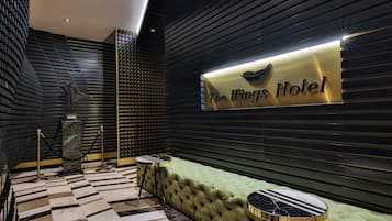 Un hall de hotel con un sofá tapizado de verde, una mesa de centro con estampado de mármol y un letrero que dice 'The Wings Hotel'.