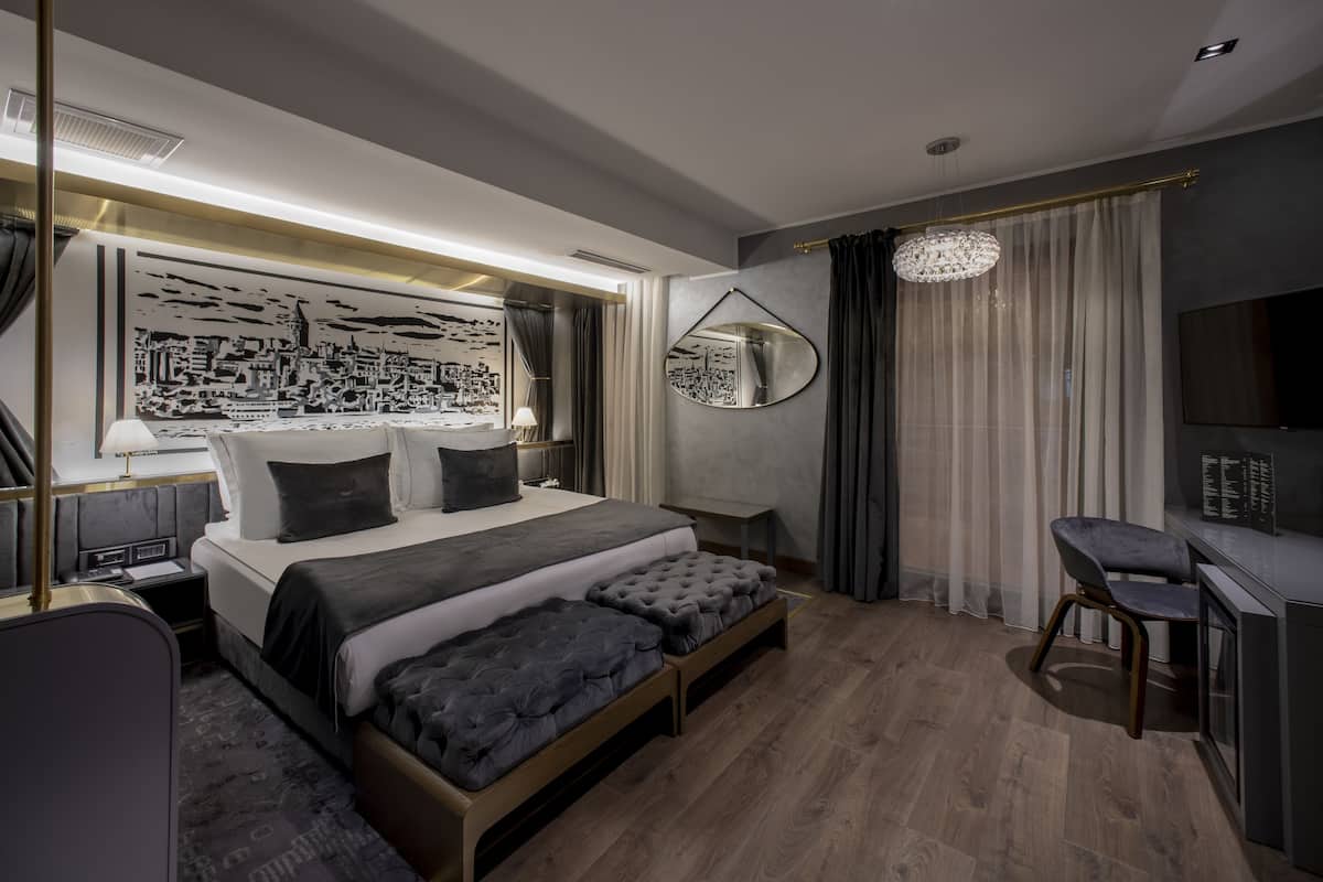 Una habitación de hotel moderna con una cama grande, mesitas de noche, un escritorio y una obra de arte con vistas a la ciudad.