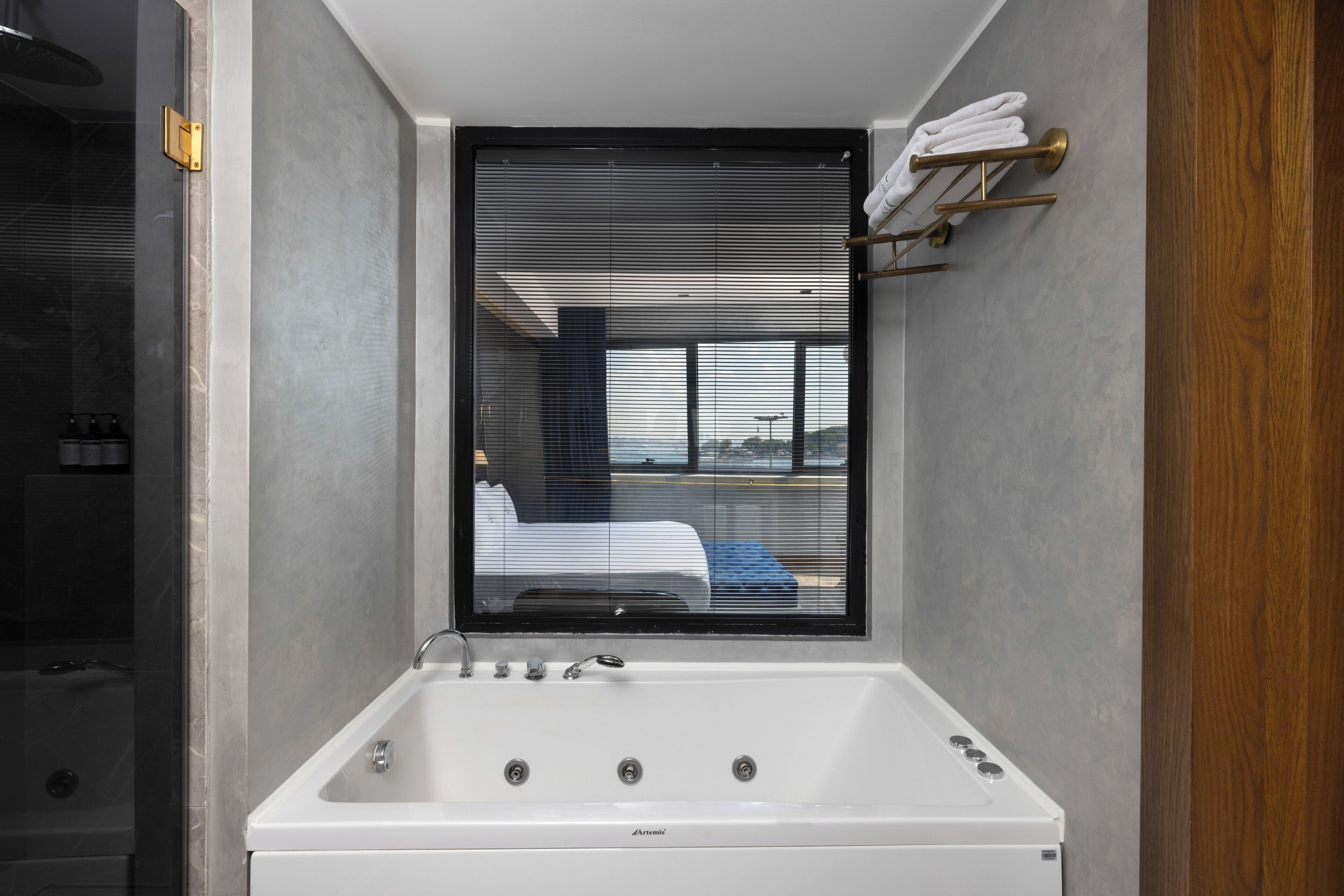 Une salle de bain moderne avec une grande baignoire, une fenêtre avec des stores et un porte-serviettes.
