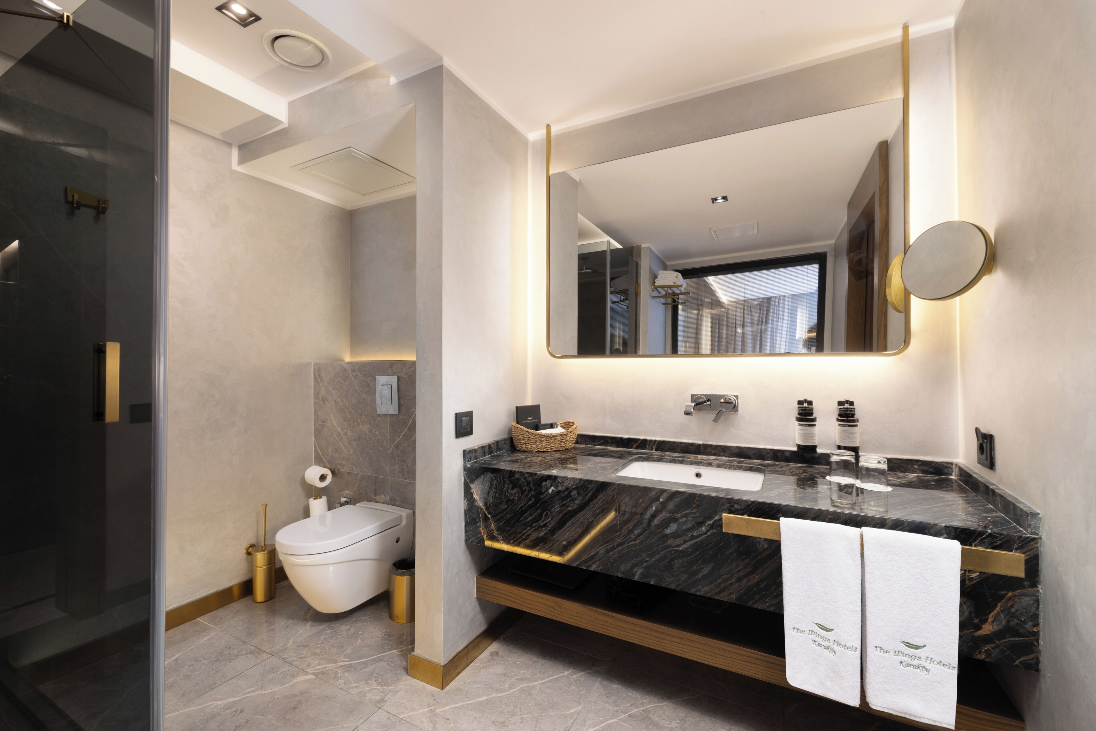 Ein modernes Badezimmer mit Marmorplatte, großem Spiegel und Toilette.