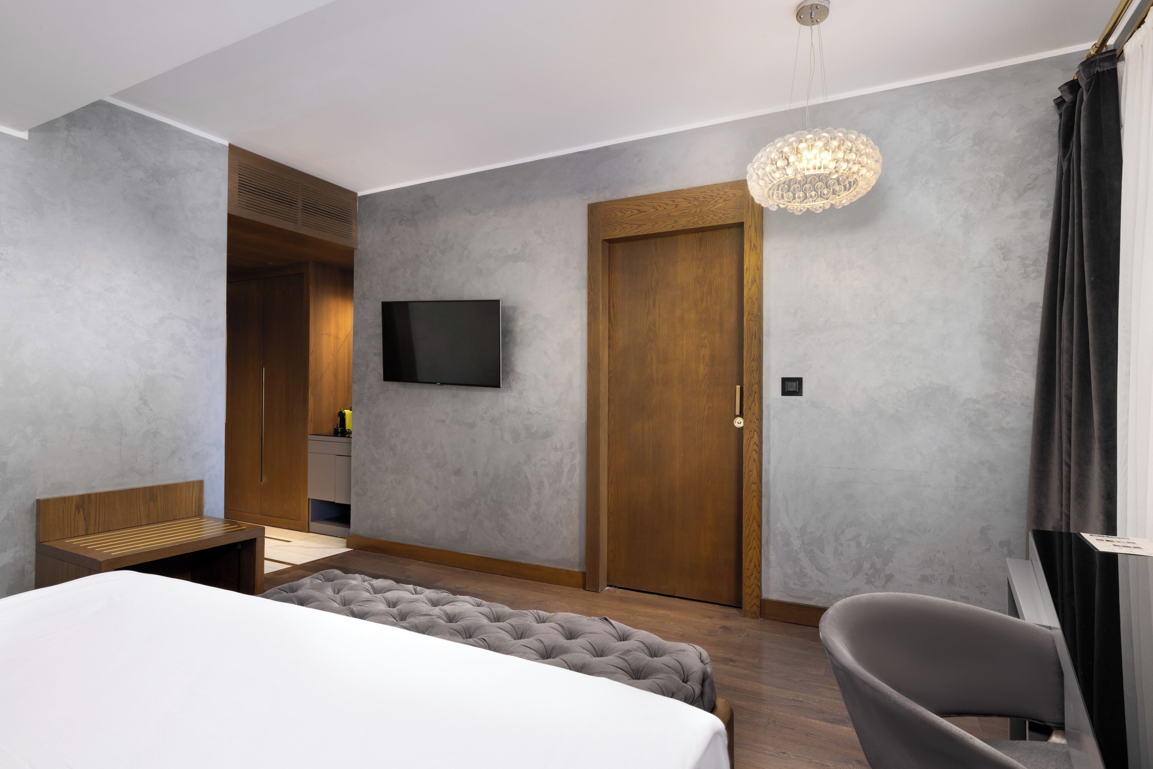Quarto de hotel moderno com uma cama grande, um espaço de estar, uma televisão e um candelabro.