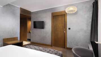 Quarto de hotel moderno com uma cama grande, um espaço de estar, uma televisão e um candelabro.