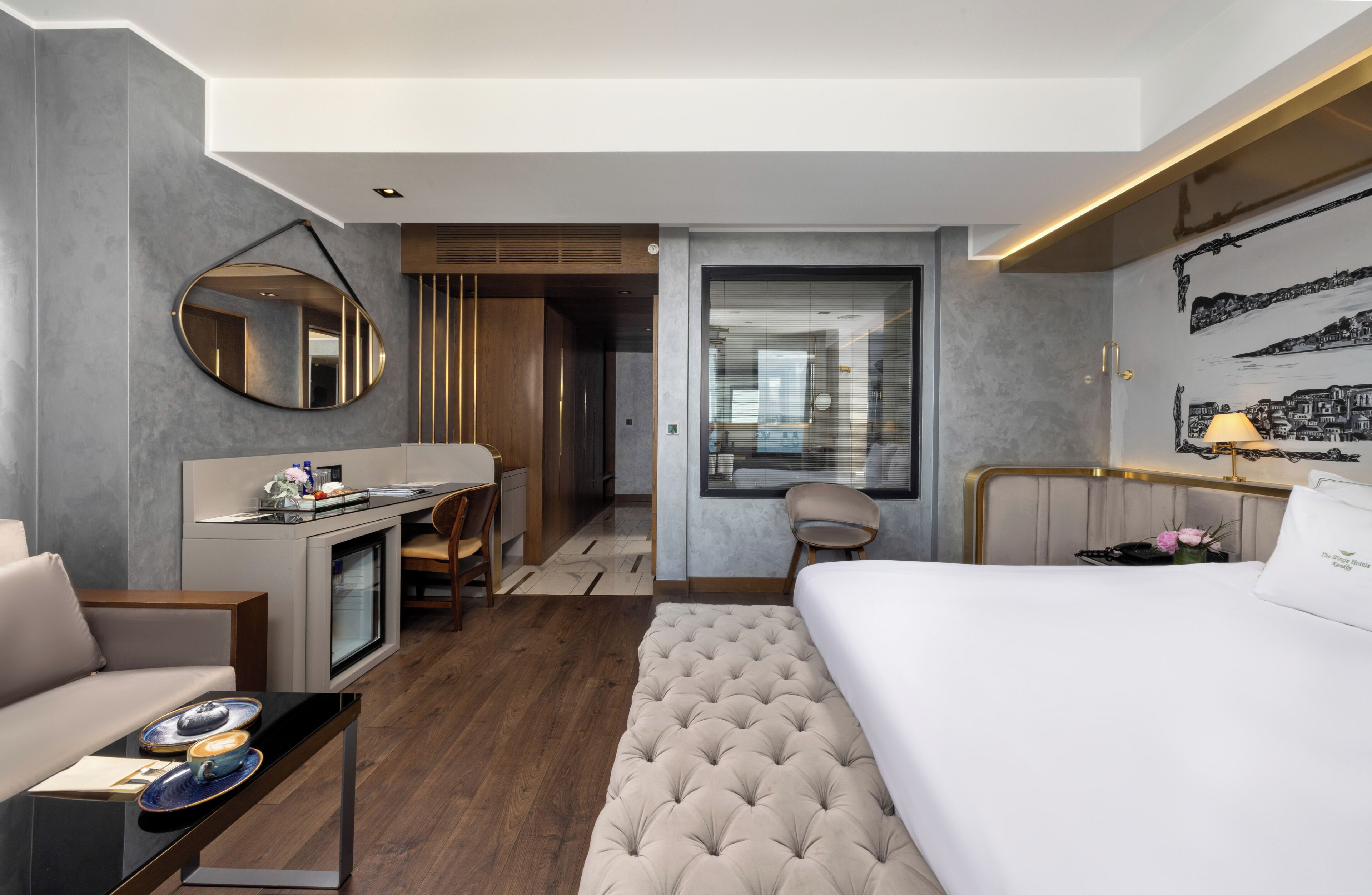 Een moderne hotelkamer met een bed, bureau, stoel en een grote spiegel.