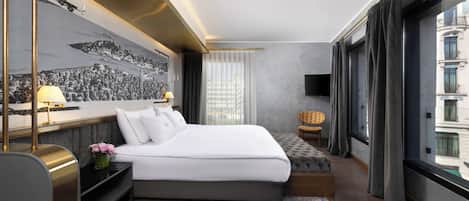 A modern hotel room with a large bed, a desk, a chair, a flat-screen TV, and a cityscape mural on the wall.