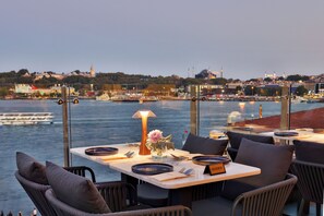 A dining table set with plates, cutlery, and a candle, overlooking a waterfront with boats and cityscape in the background. - The Wings Hotels Karakoy (Istanbul)