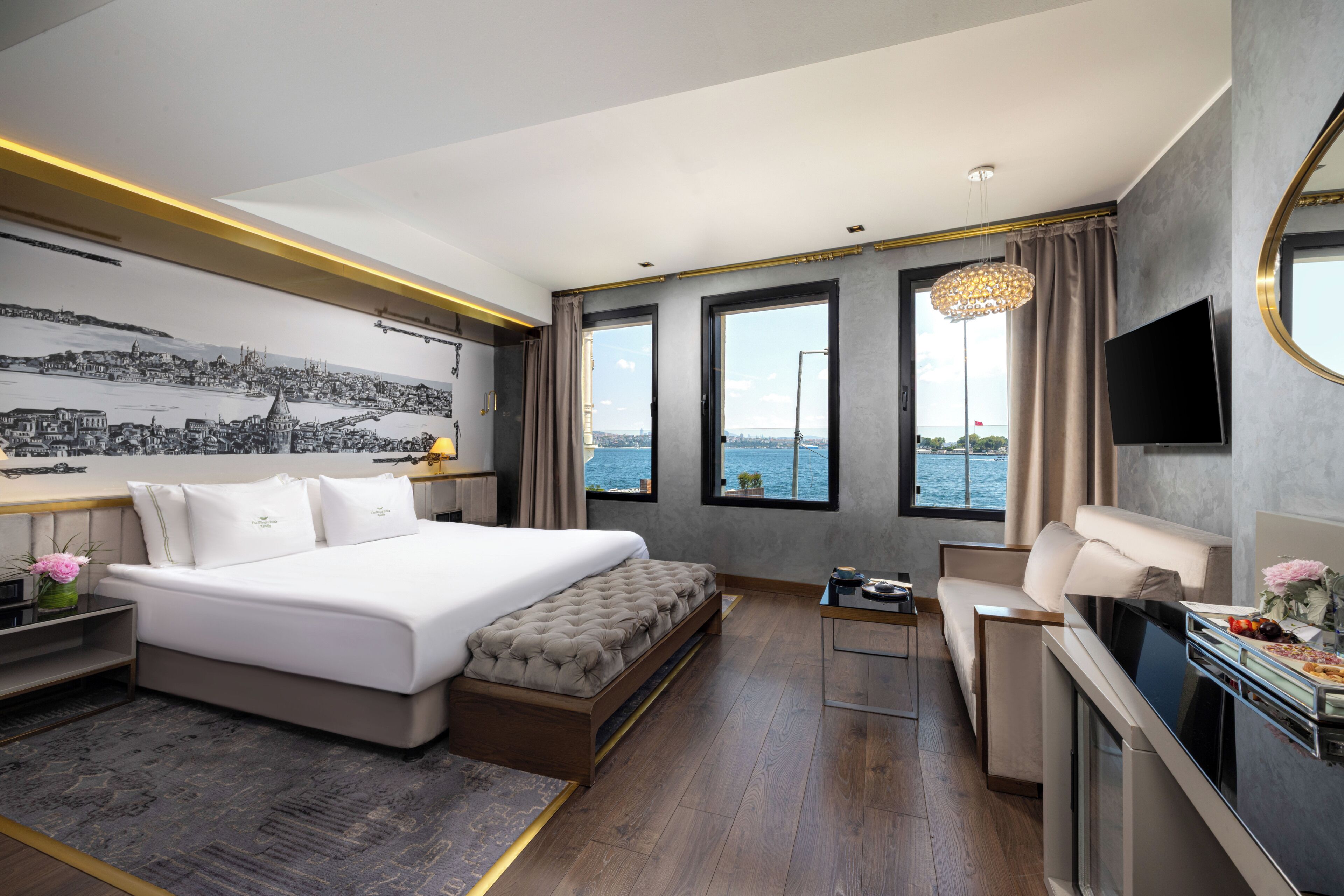 A modern hotel room with a large bed, a desk, a seating area, and a view of the sea.