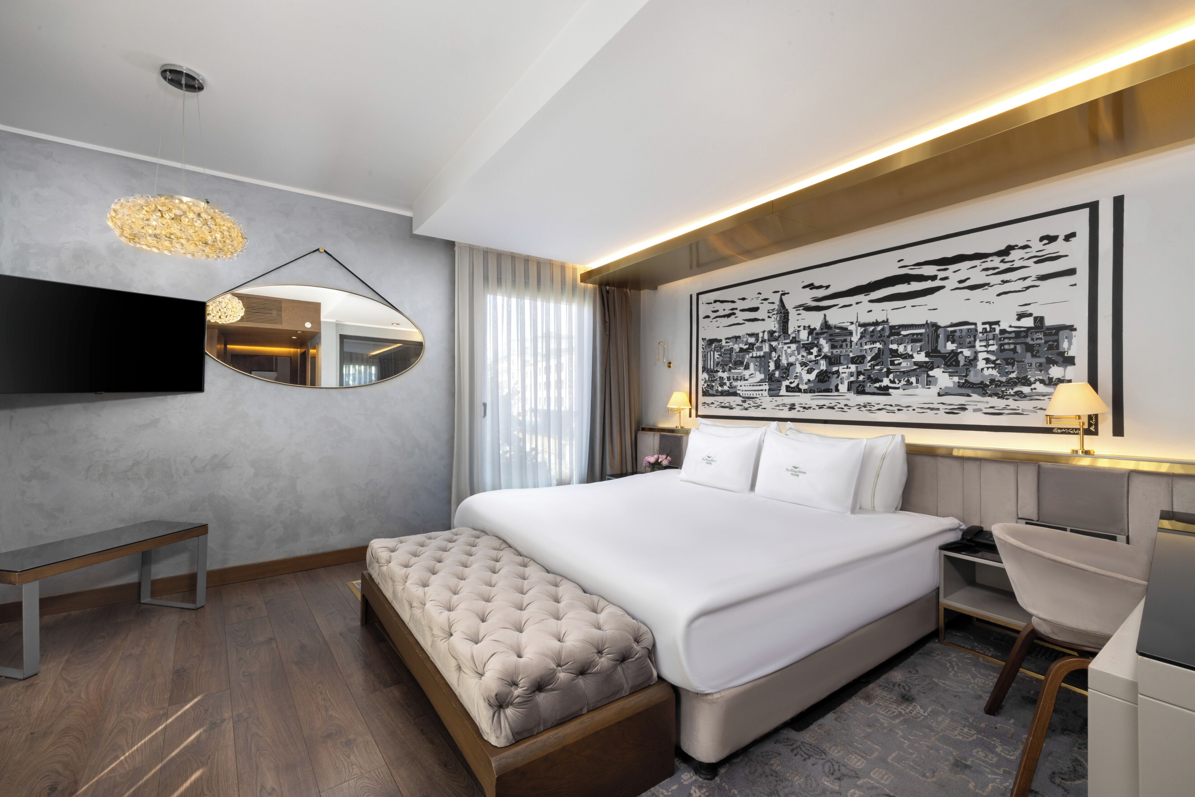 A modern hotel room with a large bed, a flat-screen TV, a bedside table, a chair, and a large cityscape artwork on the wall.