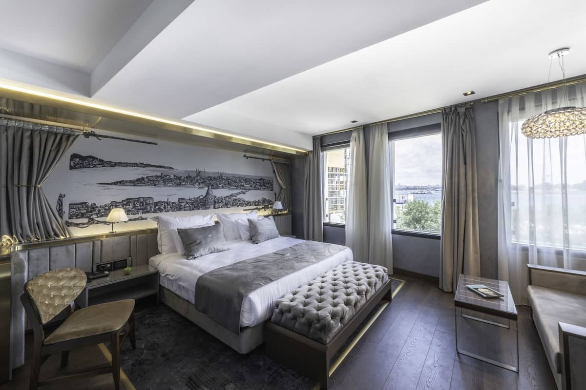 Un hotel moderno con una cama grande, vistas de la ciudad por la ventana, un mural urbano en la pared y vistas de la ciudad desde el ventanal.