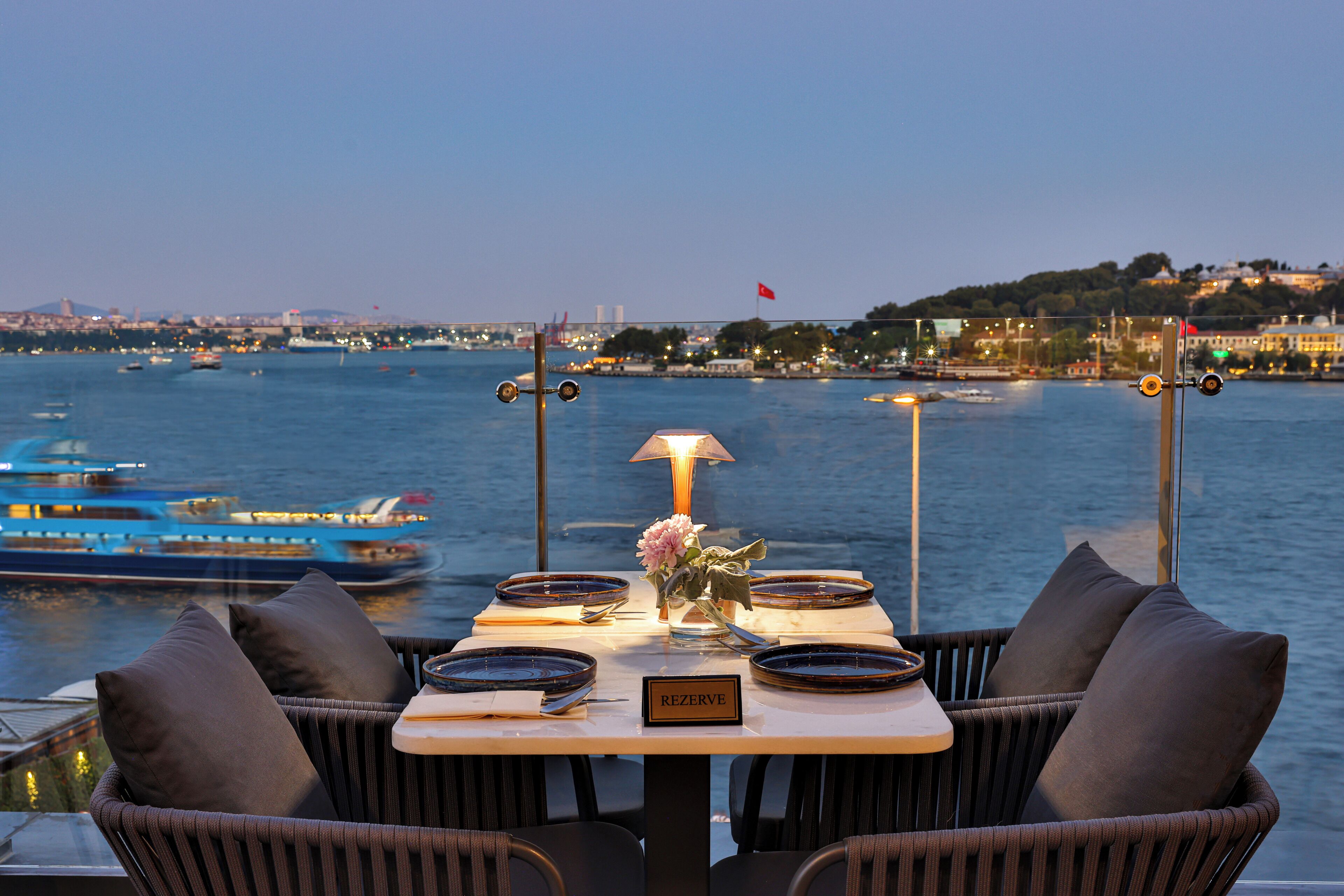 Une table dressée pour deux personnes, avec vue sur l’eau et le paysage urbain.