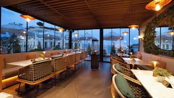 A restaurant with outdoor seating, large windows, and a view of the cityscape.