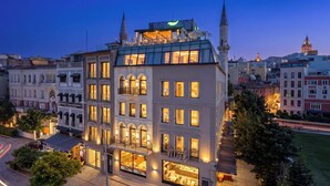 A multi-story hotel with a prominent green sign on the roof, large windows, and a visible restaurant on the ground floor. - The Wings Hotels Karakoy (Istanbul)