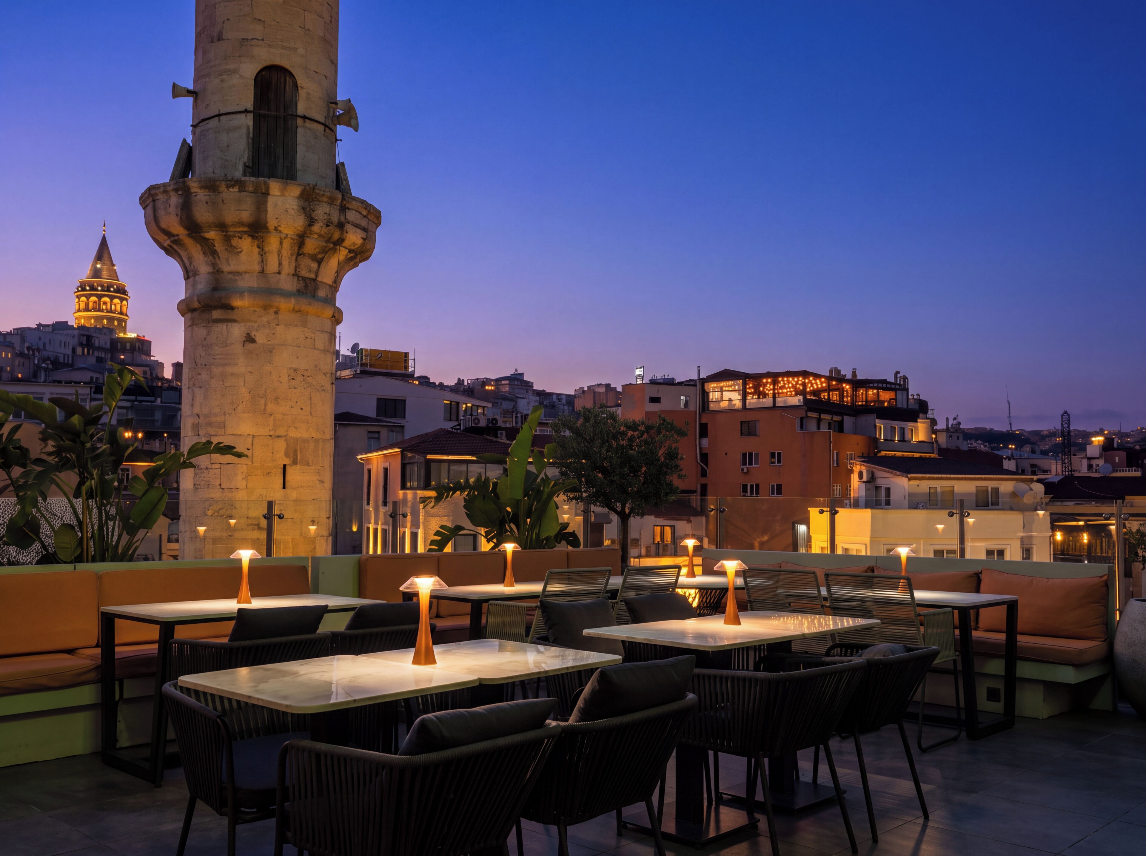 An outdoor seating area with tables and chairs, a stone column, and a cityscape in the background.