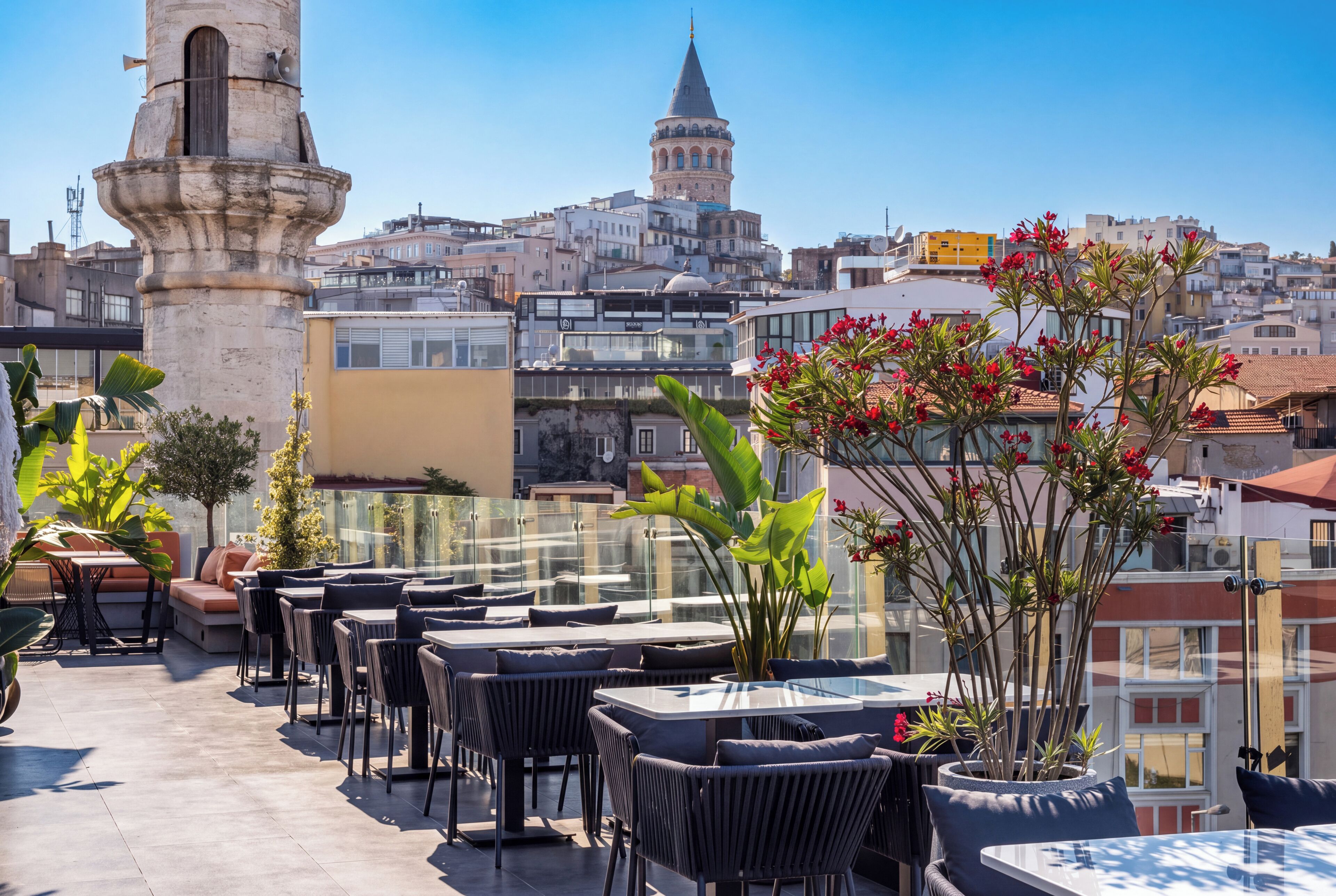 An outdoor seating area with tables and chairs, a stone column, and a view of a cityscape with a prominent tower.