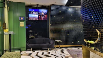 A modern hotel lobby with a large flat-screen TV, a sofa, a patterned rug, and a unique wall design.