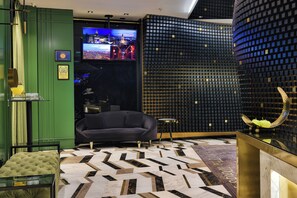 A modern hotel lobby with a large flat-screen TV, a sofa, a patterned rug, and a unique wall design. - The Wings Hotels Karakoy (Istanbul)