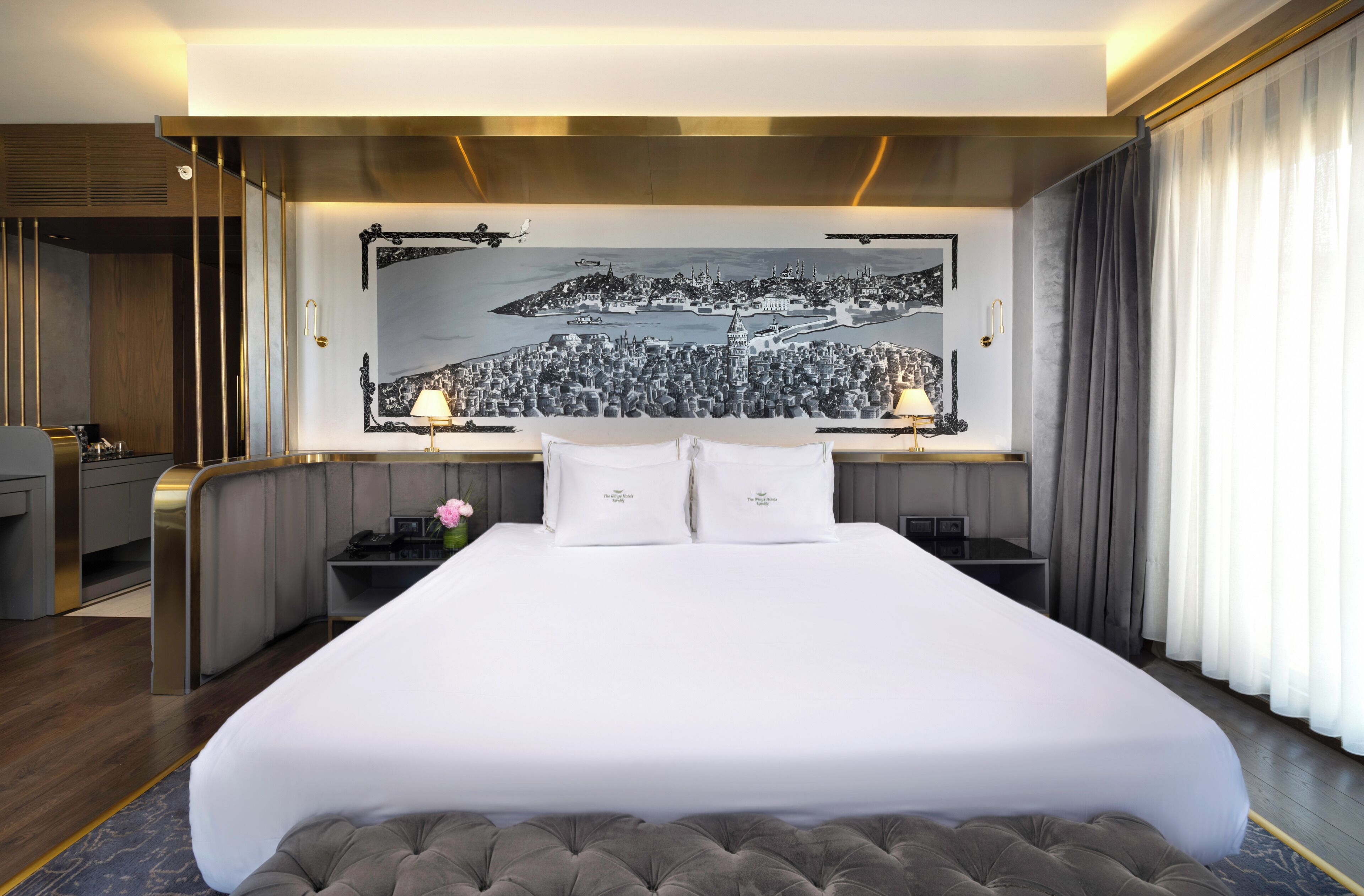 A hotel room with a large bed, two bedside lamps, a nightstand, a desk with a telephone, and a large wall mural.