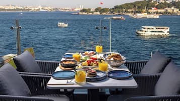 A table set with breakfast overlooking a body of water with boats and a distant cityscape.