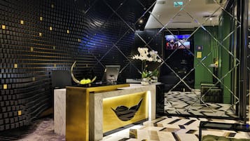 Uma área de recepção com design moderno, destacando um balcão de mármore, paleta de cores preta e dourada e piso estampado.