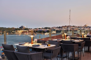 An outdoor dining area with tables and chairs, overlooking a body of water and a cityscape with buildings and a mosque. - The Wings Hotels Karakoy (Istanbul)