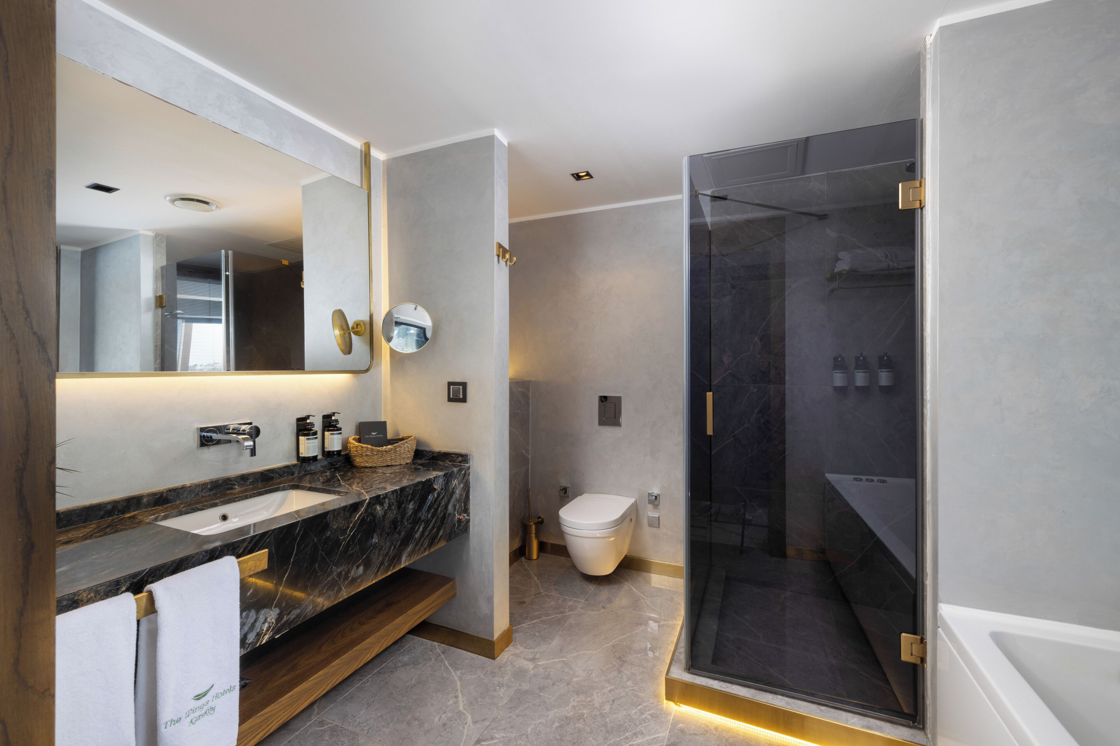 Un bany modern amb un lavabo de marbre, un mirall gran, dutxa amb envidriera i un vàter.