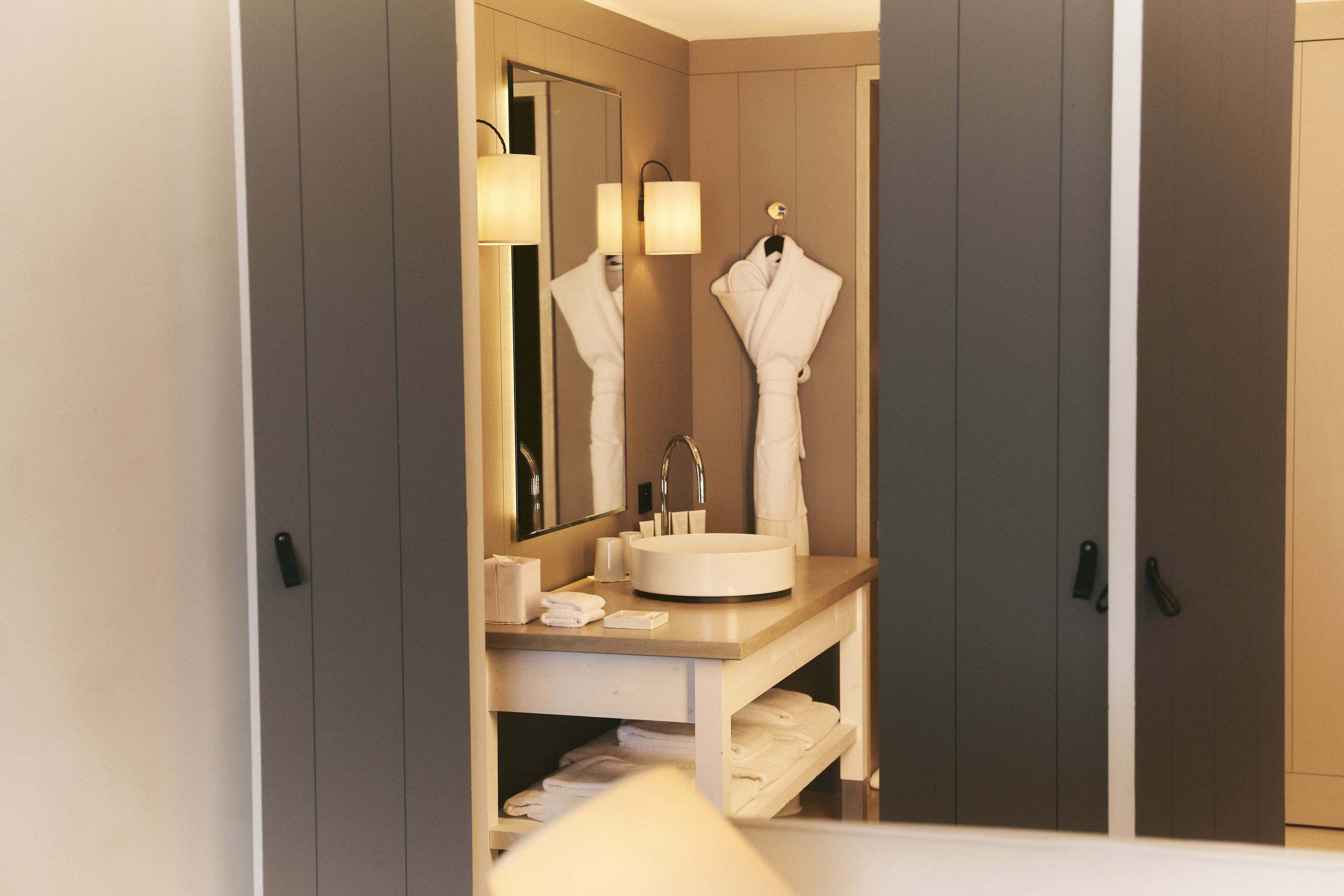 A hotel bathroom with a sink, mirror, towel rack, and a towel dispenser.
