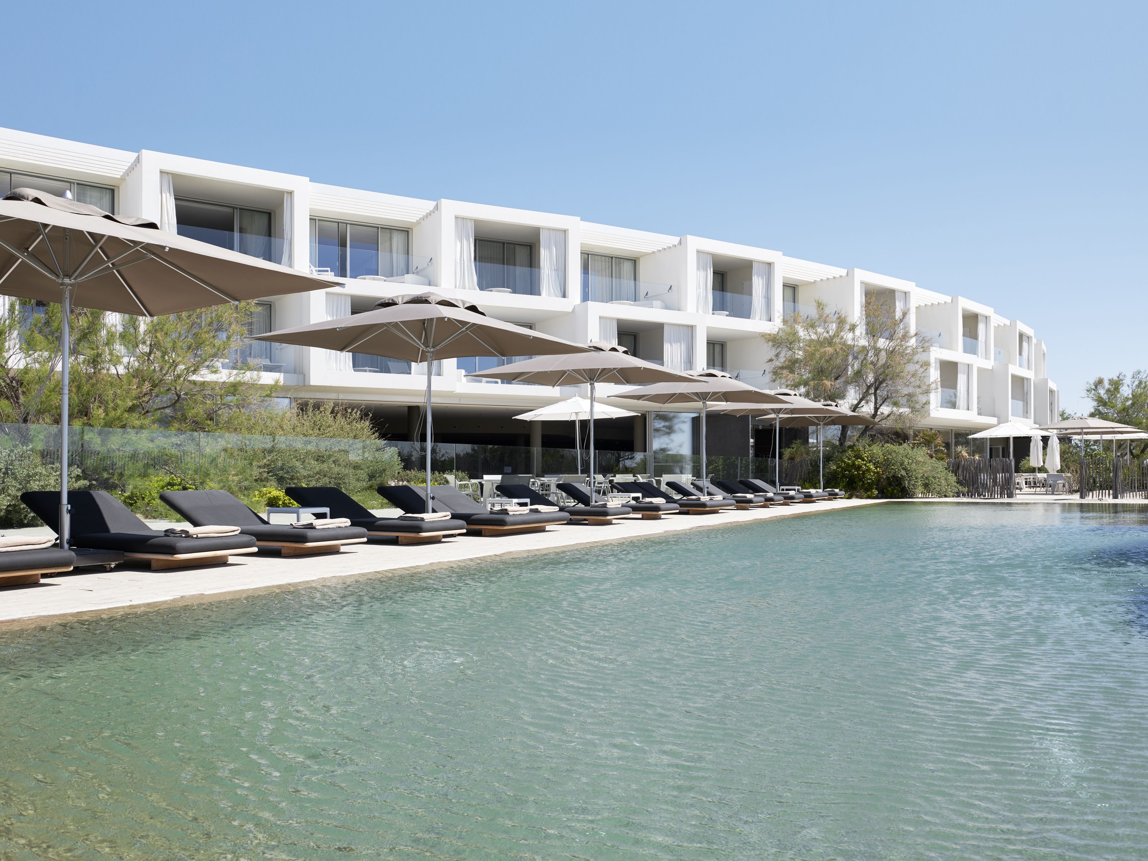 A modern hotel with a poolside lounge area, sun umbrellas, and a clear view of the pool.