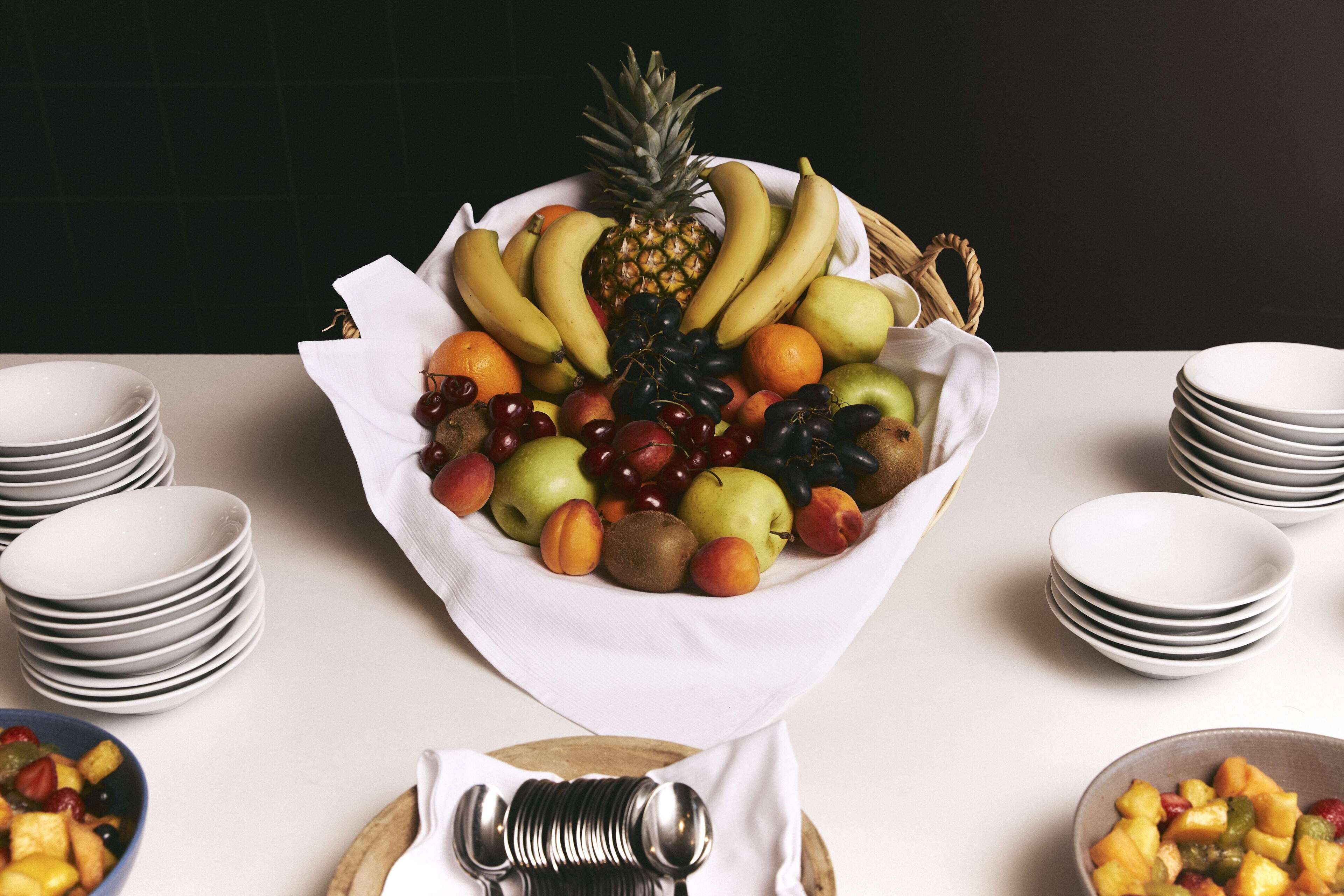 A fruit bowl on a table with stacks of white plates and a blue bowl of fruit.