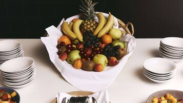 A fruit bowl on a table with stacks of white plates and a blue bowl of fruit.