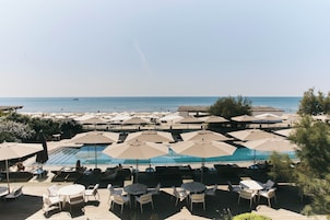 A poolside area with multiple umbrellas and lounge chairs, overlooking a clear blue sea.