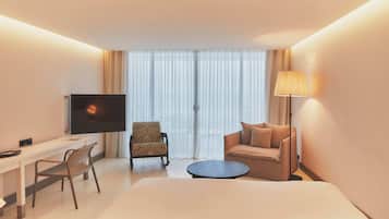 Habitación de hotel con cama, escritorio con televisor, sillón, sofá y lámpara.